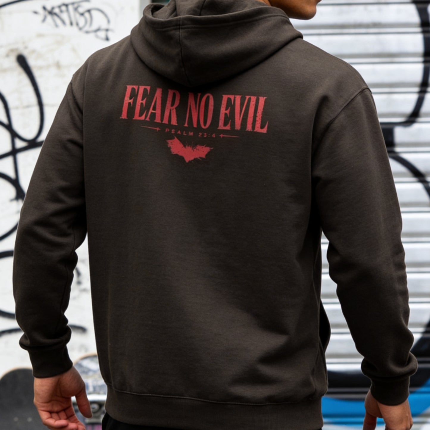 Person wearing a hoodie with 'Fear No Evil' text on the back against a graffiti-covered wall.