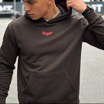 Person wearing a dark hoodie with a red logo on a blurred background